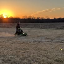 Zero-turn mower cutting a frosty open field at sunrise