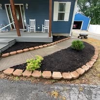 Finished curved mulch bed with stone-block edging and new shrubs along a front walkway