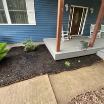 Fresh mulch bed being installed along the front porch of a blue house